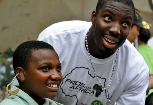 Esta fotografía tomada el 21 de marzo de 2011 muestra al Vontae Davis, entonces defensa de los Miami Dolphins, levantar la vista para consultar con su intérprete mientras le coloca un audífono a un niño en Musanze, Ruanda (Foto: Steve Terill / AFP)